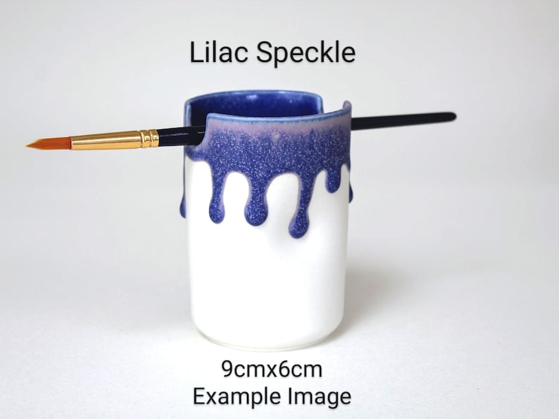 May include: A white ceramic brush holder with a blue and purple speckled glaze. The glaze drips down the sides of the holder. The holder is 9 cm by 6 cm. Lilac Speckle Example Image