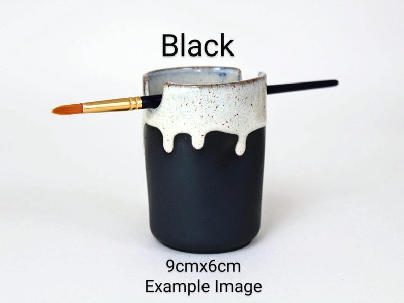 May include: Black ceramic brush holder with a white drip glaze. The holder is 9cm x 6cm and has a brush resting on the rim.