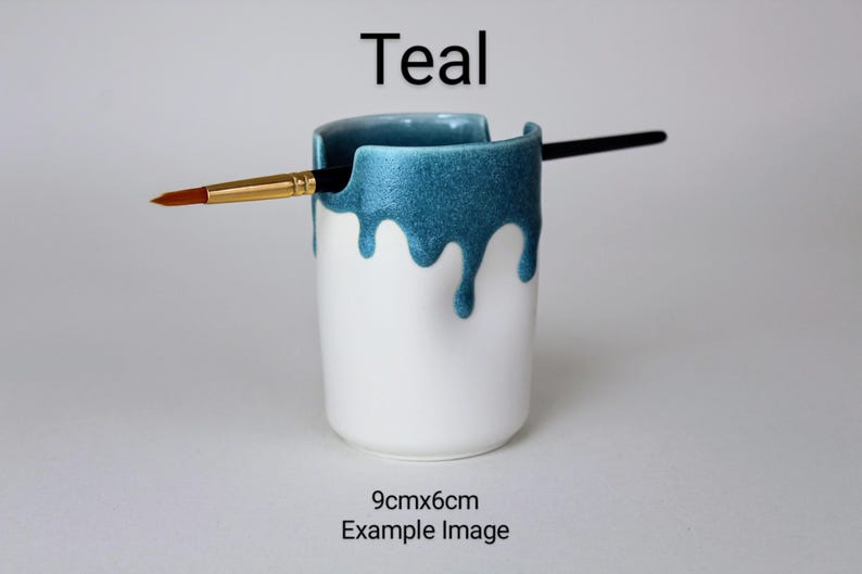 May include: Teal ceramic brush holder with a drip glaze design. The holder is 9cm x 6cm and is shown with a paintbrush.