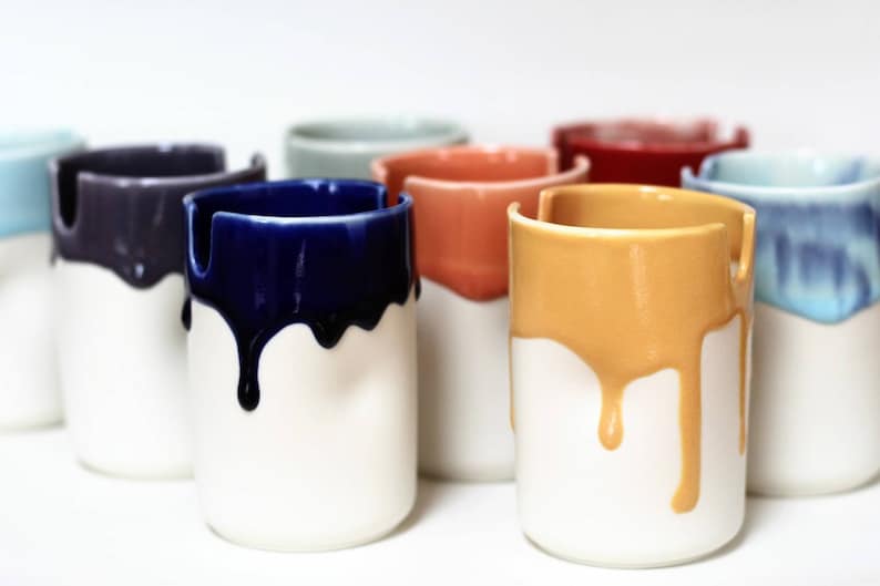 May include: A set of eight ceramic mugs with a white base and a colored glaze that drips down the sides. The colors include blue, purple, green, orange, red, yellow, and light blue.