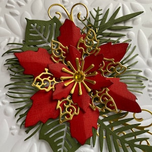 May include: A red poinsettia flower with gold accents and green leaves. The flower is made of paper and has a sparkly center.