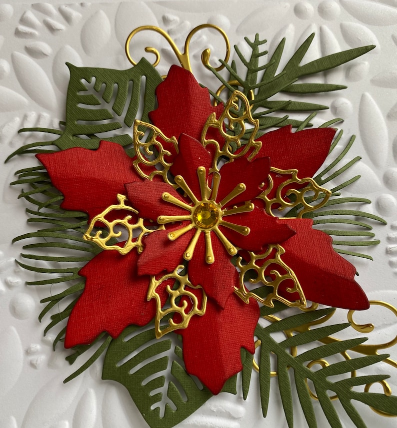 May include: A red poinsettia flower with gold accents and green leaves. The flower is made of paper and has a sparkly center.