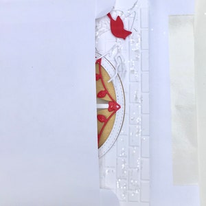 May include: A white card with a red cardinal and a gold and red decorative element. The card is partially inside a white envelope.