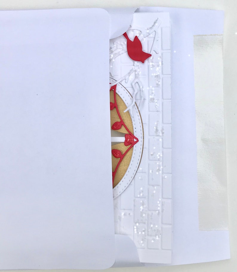 May include: A white card with a red cardinal and a gold and red decorative element. The card is partially inside a white envelope.