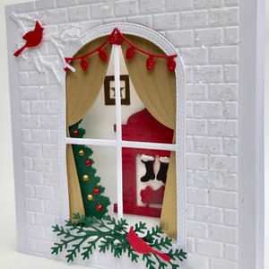 May include: A white brick wall with a window cut out. The window has a red and white house with a Christmas tree inside. There are red cardinals on either side of the window.