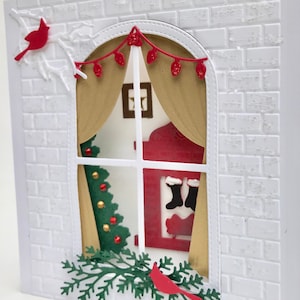 May include: A white card with a red cardinal, a window with a Christmas tree, a fireplace with stockings, and a garland of lights. The window is framed by a brick wall.