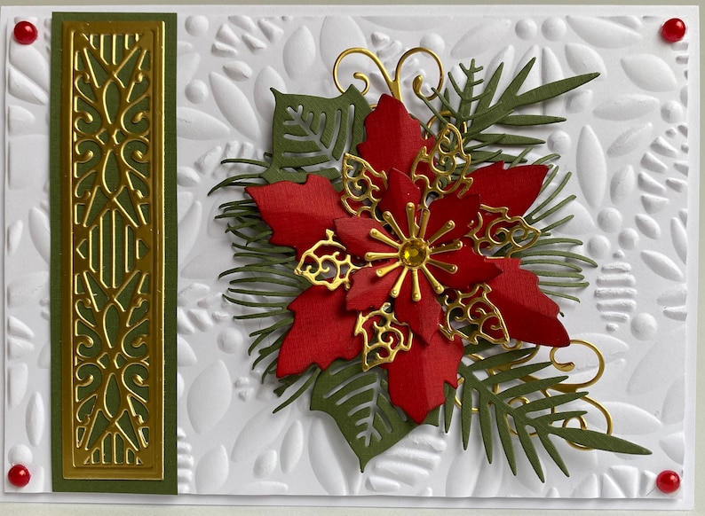 May include: A Christmas card with a red poinsettia flower, green leaves, and gold accents. The card has a white background with a textured pattern.