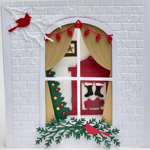 May include: A white brick wall with a window cut out. The window has a red and gold curtain, a red fireplace, and a Christmas tree with red and gold ornaments. There are two red cardinals and a green garland with red berries.