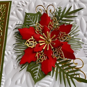May include: A red poinsettia flower with gold accents and green leaves on a white background. The flower is surrounded by a decorative border of gold and green.