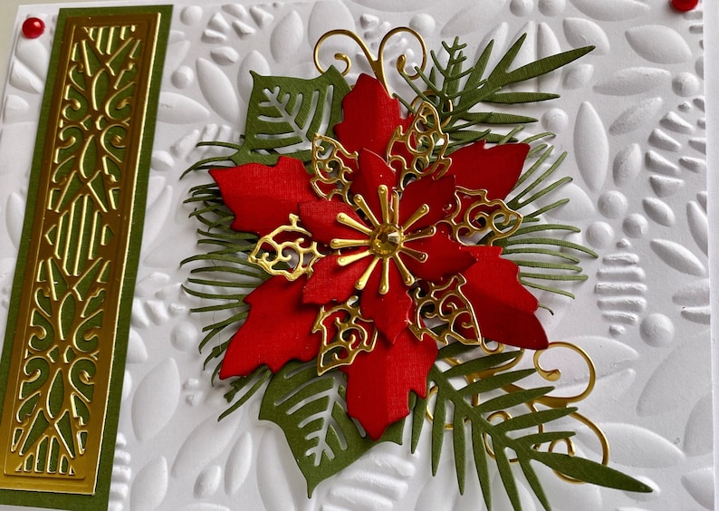 May include: A red poinsettia flower with gold accents and green leaves on a white background. The flower is surrounded by a decorative border of gold and green.