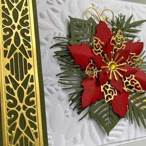 May include: A handmade Christmas card featuring a red poinsettia with gold accents and green foliage. The card has a white background with an embossed pattern and a gold and green border.