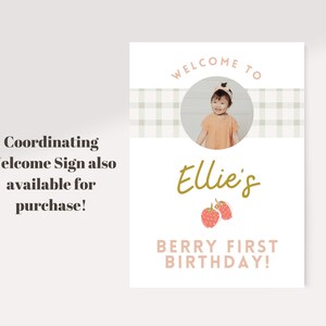 May include: A welcome sign for a first birthday party. The sign features a photo of a child, the name "Ellie's" in gold script, and the text "Berry First Birthday!" in pink. The sign also includes the text "Coordinating Welcome Sign also available for purchase!"