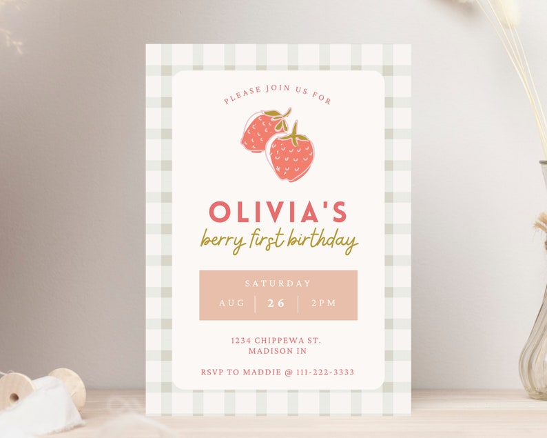 May include: A light pink and cream-colored invitation card with a gingham border. The card features the text "OLIVIA'S berry first birthday" with a strawberry illustration. The date and time are also included.