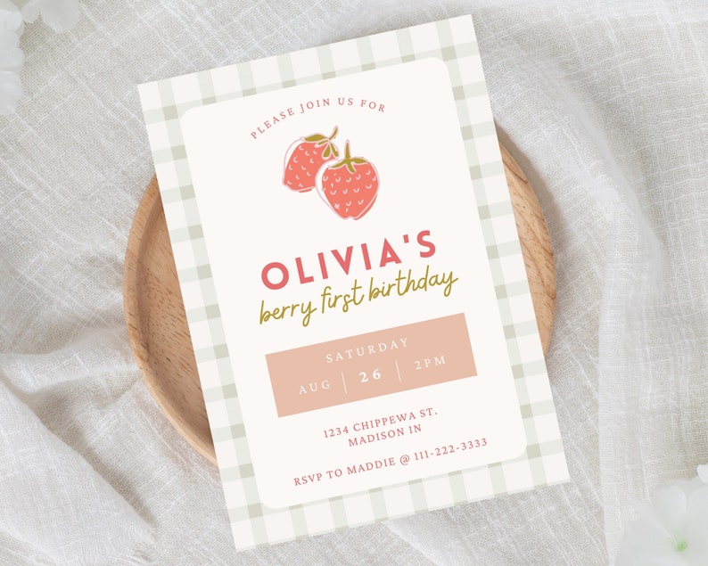 May include: A birthday invitation with a strawberry theme. The invitation features the text "OLIVIA'S berry first birthday" in pink and green. The date and time are displayed in a pink rectangle. The background has a light green and white gingham pattern.