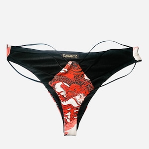 Può includere: Intimo a fantasia nero e rosso con un design a bretelle incrociate e la scritta "CANARYZ" stampata sul davanti.
