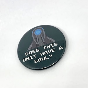 Może przedstawiać: Czarno-biały guzik z twarzą robota i tekstem "DOES THIS UNIT HAVE A SOUL?"