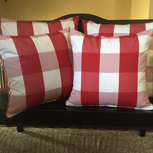 May include: Four red and white gingham throw pillows on a black bench. The pillows are arranged in a staggered pattern.