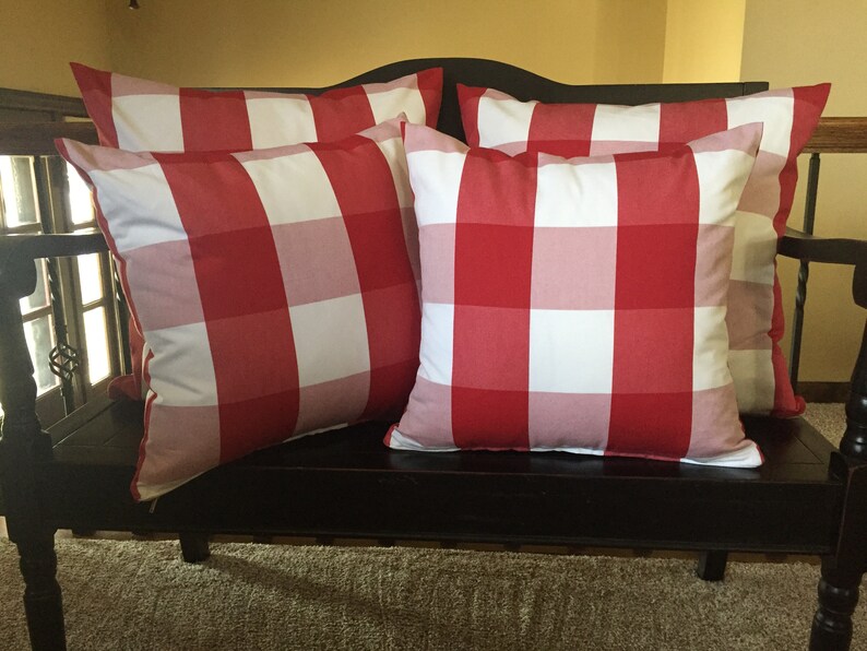 May include: Four red and white gingham throw pillows on a black bench. The pillows are arranged in a staggered pattern.