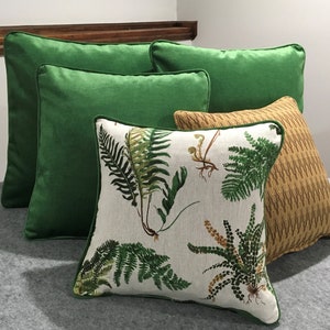 May include: Four decorative throw pillows, two are solid green, one is a light brown with a subtle pattern, and one is white with a green fern pattern.