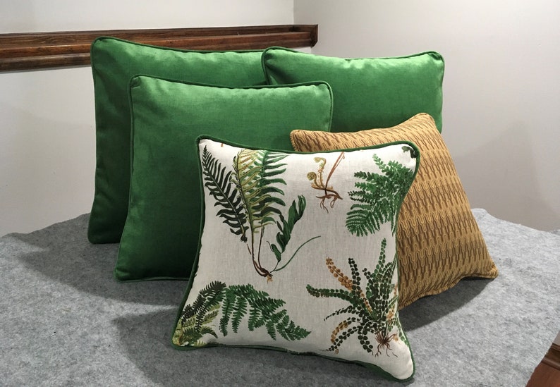May include: Four decorative throw pillows, two are solid green, one is a light brown with a subtle pattern, and one is white with a green fern pattern.
