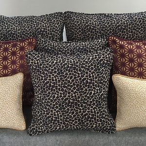 May include: A set of eight decorative throw pillows with various patterns. The pillows feature a leopard print, a geometric pattern, and a speckled pattern. The pillows are in shades of brown, beige, and gold.