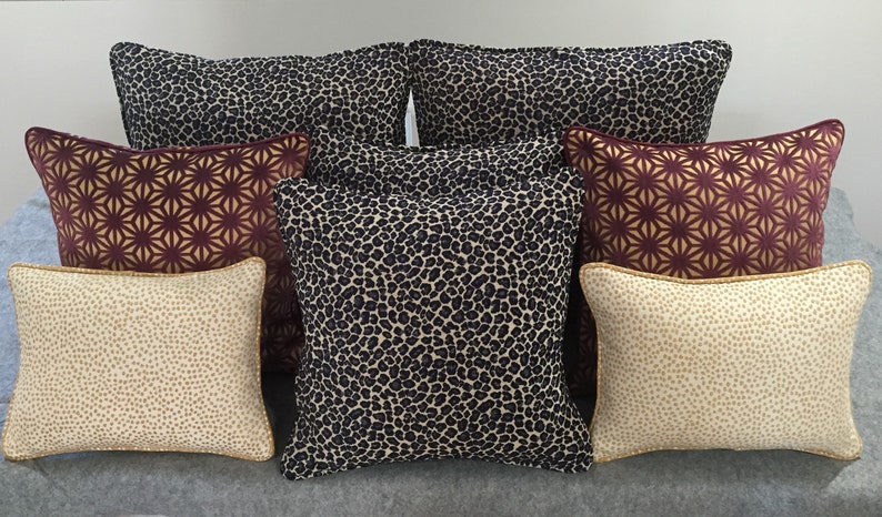 May include: A set of eight decorative throw pillows with various patterns. The pillows feature a leopard print, a geometric pattern, and a speckled pattern. The pillows are in shades of brown, beige, and gold.