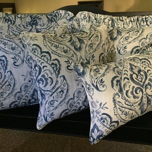 May include: Four decorative throw pillows with a blue and white paisley pattern. The pillows are arranged on a black bench.