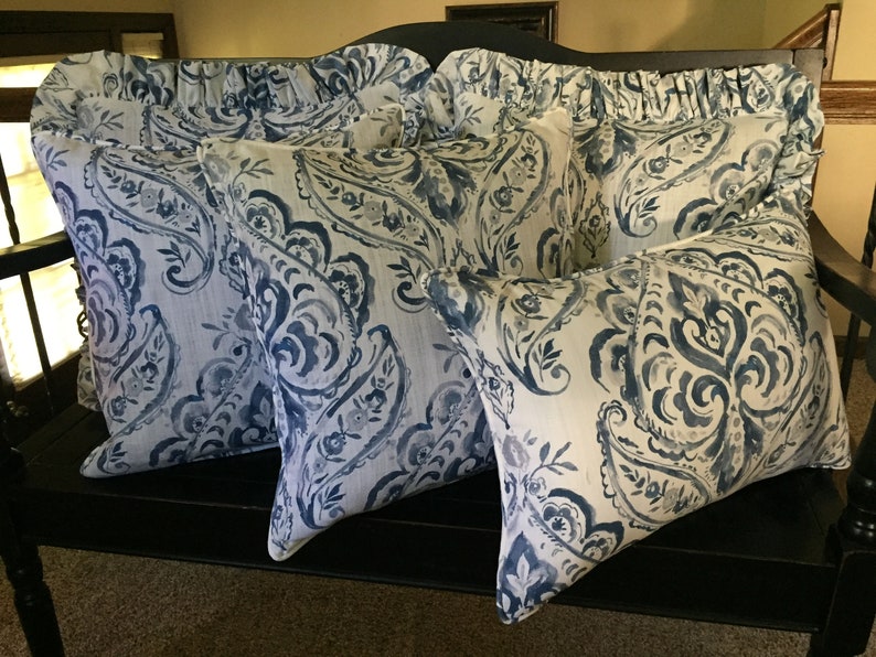 May include: Four decorative throw pillows with a blue and white paisley pattern. The pillows are arranged on a black bench.