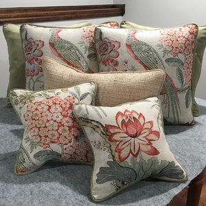 May include: Five decorative throw pillows with floral and bird patterns. The pillows are arranged on a light gray surface. The pillows are in shades of green, red, and white.