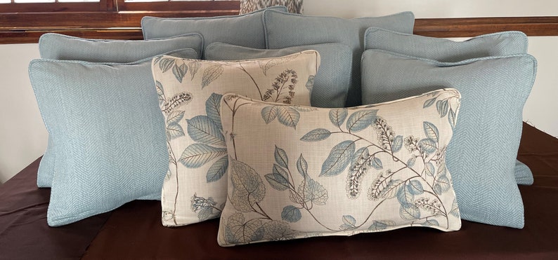 May include: A group of decorative throw pillows in a variety of patterns and colors. The pillows are arranged on a brown couch. The pillows are made of a soft, comfortable fabric and feature a variety of designs, including floral patterns and solid colors.