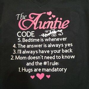 Peut inclure: T-shirt noir à col en V avec un texte blanc qui dit "The Auntie Code" et une liste de règles pour être une tante. Le texte comprend des cœurs et un motif floral.