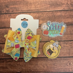 Può includere: Un fiocco di glitter giallo e oro con una stampa di forniture scolastiche. Il fiocco è attaccato a una carta bianca con il testo "Tie it with a B-Bow". Ci sono due toppe da stirare, una con il testo "School Time" e l'altra con una sveglia dei cartoni animati.