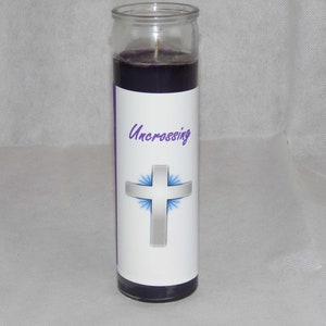Könnte beinhalten: Lilafarbene Glaskerze mit einem weißen Etikett, auf dem "Uncrossing" steht, und einem silbernen Kreuz mit blauen Strahlen, die von ihm ausgehen.