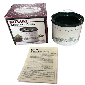 May include: A Rival Potpourri Crock electric simmering cooker with a white ceramic exterior and a dark green interior. The crock features a floral design and comes with its original box and instructions.