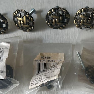 May include: Antique brass cabinet knobs with a woven design. The knobs are 1 1/2 inches in diameter. The image also shows the knobs in their original packaging, with the text "KNOB ANT BRASS 1 1/2IN".