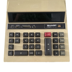 May include: A vintage Sharp Compet OS-2122 calculator with a beige body and black keys. The calculator features a black display screen and red, black, and white buttons. The calculator has a 12-digit display.