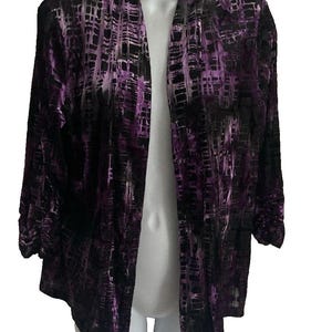 May include: A purple and black open-front jacket with a textured pattern. The jacket is displayed on a white mannequin, showcasing its design and style. The sleeves are three-quarter length.