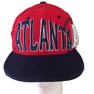May include: Red and blue baseball cap with the word "ATLANTA" embroidered in white on the front. The cap has a black brim.