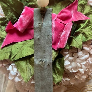 May include: A white and brown pin with a pearl-like top. The pin is attached to a gray fabric ribbon with holes.