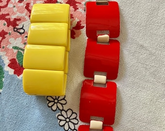 May include: Two vintage plastic bracelets, one yellow and one red. The bracelets are made of interlocking squares.