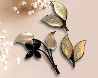 May include: A silver brooch with a black flower and leaves. The leaves are silver with a white enamel finish.