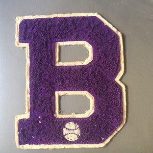 May include: Purple felt letter B with a white outline and a white baseball graphic in the center.