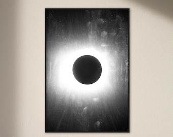 May include: A black and white abstract art print featuring a black circle with a white halo, resembling a solar eclipse. The background is a dark grey with a textured, brushstroke effect.