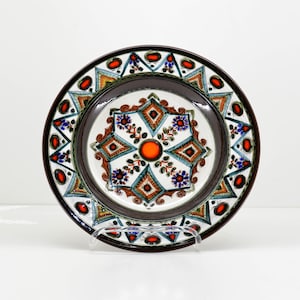 May include: A ceramic plate with a brown rim and a white center featuring a geometric design with orange, blue, and green accents.