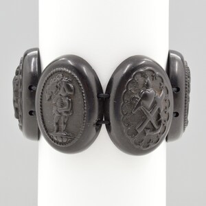 May include: A black jet bracelet with five oval-shaped links. Each link features a different carved design, including a cherub, a heart, an anchor, and two floral designs.