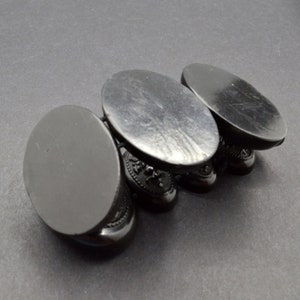 May include: Four black oval-shaped display stands with intricate designs. The stands are stacked on top of each other.