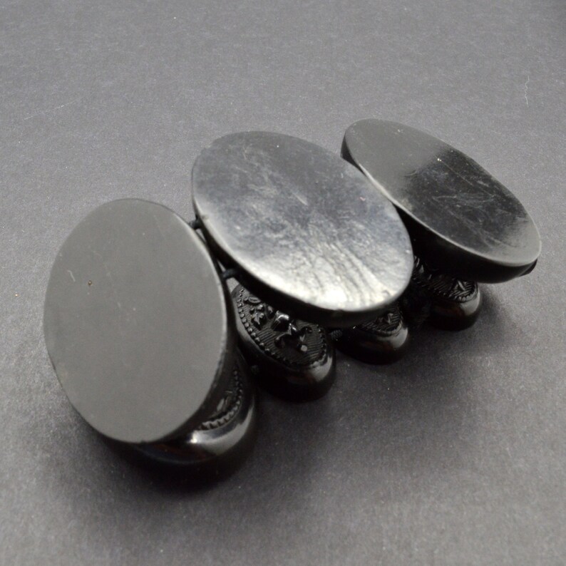 May include: Four black oval-shaped display stands with intricate designs. The stands are stacked on top of each other.
