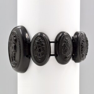 May include: Black jet bracelet with oval-shaped links featuring raised, carved designs. Each link is connected by a black elastic cord.