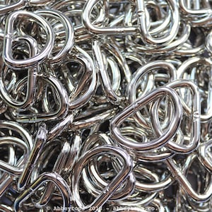 May include: A pile of silver metal D-rings. The rings are all the same size and shape, and they are arranged in a random pattern.