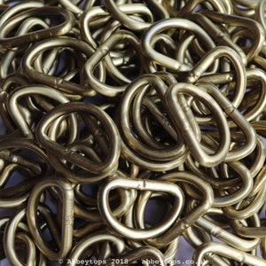 May include: A pile of gold-colored metal D-rings. The rings are all the same size and shape, and they are arranged in a random pattern.